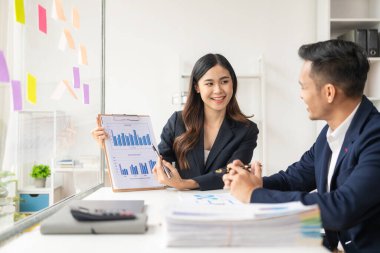 Zeki ve profesyonel erkek yönetici, bayan asistanıyla çalışıyor. Mali raporları grafik kağıtları ve masaüstü bilgisayarlarla analiz et.