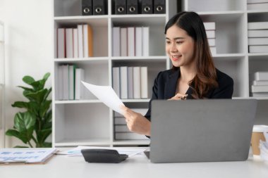 Asyalı kadın muhasebeci, istatistik ve analitik araştırma konseptiyle birlikte dizüstü bilgisayarla çalışan şirket çalışanlarının maaşlarını ödüyor..