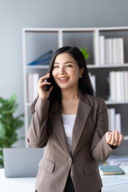Modern ofiste elinde kalemle gezen mutlu Asyalı iş kadını resmi takım elbiseli, mutlu ve neşeli dikey imajlı bir bayan.