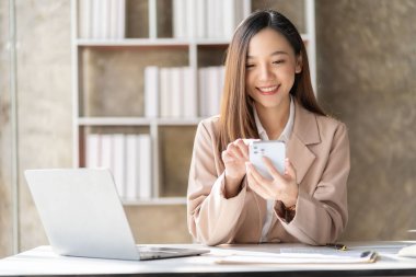 Akıllı telefon ve dizüstü bilgisayarla çalışan güzel Asyalı kadın muhasebeci iş raporlarını ve belgeleri analiz ediyor. Akıllı telefondan mesaj göndermek ya da sohbet etmek
