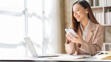 Akıllı telefon ve dizüstü bilgisayarla çalışan güzel Asyalı kadın muhasebeci iş raporlarını ve belgeleri analiz ediyor. Akıllı telefondan mesaj göndermek ya da sohbet etmek
