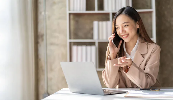 stock image Beautiful Asian female accountant working with smartphone and laptop at her desk analyzing business reports and documents. Sending messages or chatting via smartphone on mobile