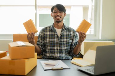 Evdeki, girişimdeki, küçük işletmedeki, KOBİ 'deki çevrimiçi satış işleri için ürünleri çevrimiçi satma talimatları alın. Paketler için ürün hazırlayan yakışıklı Asyalı adam. İnternette Fikir Satın Al