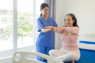 Asyalı yaşlı kadın hemşire desteğiyle fizyoterapi yapıyor. Genç kadın huzurevinde omuz kasları için fizyoterapi yapıyor.