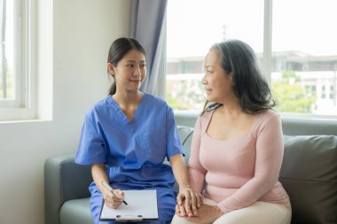60 yaşında Asyalı bir kadınla birlikte genç bir bakıcı tavsiye ve teşvik veriyor. Bir geçmiş alın ve klinikte mutlu bir şekilde yaşamak için uygun bir tedavi önerin..