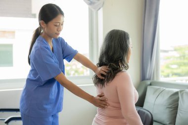 Asyalı yaşlı kadın hemşire desteğiyle fizyoterapi yapıyor. Genç kadın huzurevinde omuz kasları için fizyoterapi yapıyor.