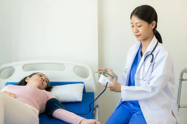 stock image Asian female nurse doctor examining senior female patient using electronic device Cardiologist measuring low blood pressure, old pensioner high blood pressure patients