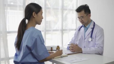 Masada oturan Asyalı bir kadın hasta steteskoplu bir tıp uzmanını dinliyor ve hastane odası sağlık sigortası konseptinde teşhis koyuyor.