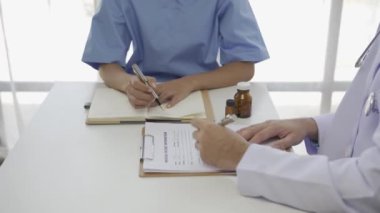 Masada oturan Asyalı bir kadın hasta steteskoplu bir tıp uzmanını dinliyor ve hastane odası sağlık sigortası konseptinde teşhis koyuyor.