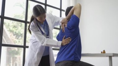 Kadın doktor erkek hastaya el kaldırmayla fizyoterapi uyguluyor, Asyalı kadın fizyoterapist çalışıyor ve hastanın elini korumaya yardım ediyor, hasta klinikte esneme hareketleri yapıyor.