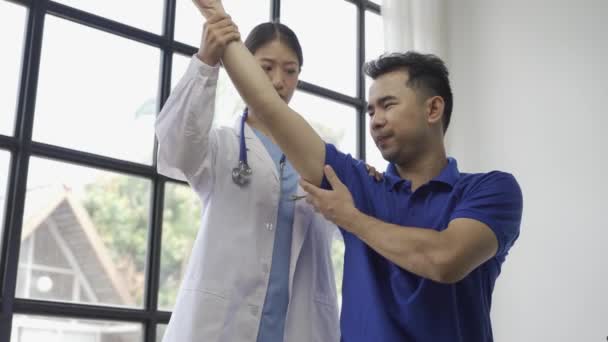 女医生用手举给予男病人理疗 亚洲女理疗师工作并帮助保护病人的手 病人在诊所做伸展运动 — 图库视频影像