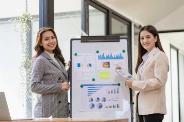 İki Asyalı iş kadını modern ofis içinde oturmuş ve danışmanlık yapıyorlar. Başlangıç projesi fikrinin sunumunu tartışıyorlar. Ofisteki istatistik ve yatırım pazarlarını analiz edin..