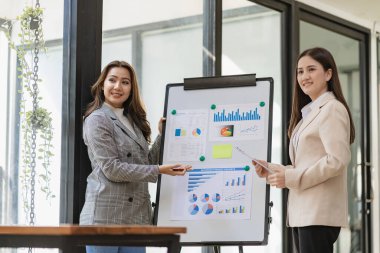 İki Asyalı iş kadını modern ofis içinde oturmuş ve danışmanlık yapıyorlar. Başlangıç projesi fikrinin sunumunu tartışıyorlar. Ofisteki istatistik ve yatırım pazarlarını analiz edin..