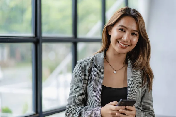 Asyalı iş kadını iş yerindeki müşterileriyle konuşurken akıllı telefon tutuyor. Hesap makinesi, iş bilgisayarı, mali muhasebeci, kredi bankası, hesap makinesi ya da doküman kullanıyor.,