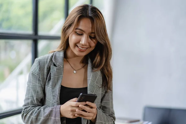 Asyalı iş kadını iş yerindeki müşterileriyle konuşurken akıllı telefon tutuyor. Hesap makinesi, iş bilgisayarı, mali muhasebeci, kredi bankası, hesap makinesi ya da doküman kullanıyor.,