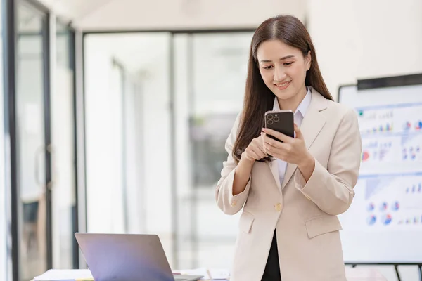 stock image Asian businesswoman holding smartphone in talking with business clients with charts or documents in workplace using calculator, business laptop, financial accountant calculating money, loan bank,