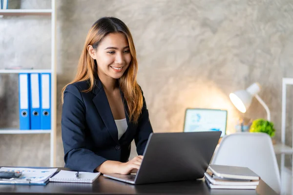 stock image Asian female entrepreneur working in finance at home office analyzing financial graphs on documents with laptop on table in office