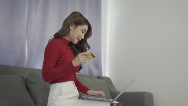 自宅のリビングルームでソファにラップトップを使用して幸せな若いアジアの女性 クレジットカードを使用してオンラインで買い物をします クレジットカードでオンラインショッピングをお楽しみください — ストック動画