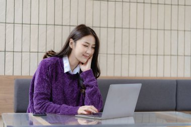 Kafede çalışan Asyalı genç bir kadın, dizüstü bilgisayar kullanan bir kadın kafede oturmuş, bilgisayarla konuşuyor bir şeyler açıkla ve internette sörf yap..