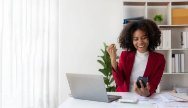 Dizüstü bilgisayarı ve finansal döküman hesap makinesiyle çalışan Afrikalı Amerikalı kız kollarını kaldırıp zaferi gülümseyerek kutlamaya hazır..