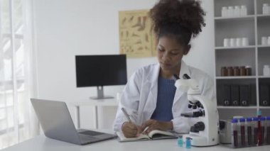 Laboratuvarda deney yapan Afrikalı kadın bilim adamı mikroskop kullanarak kan örneğine bakıyor.