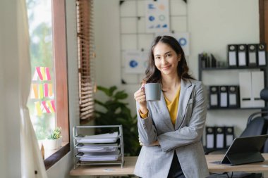 Asyalı serbest çalışan kadın elinde kahve fincanıyla internet sörfü için tabletle çalışıyor ve kafede blog yazıyor.