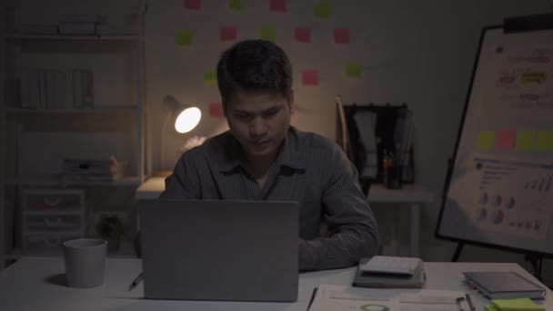 アジアの男性ビジネスマンは 財務文書やデスクトップコンピュータで働いて遅くまでオフィスで働いています 残業サラリーマンコンセプト4K働く若い男 — ストック動画