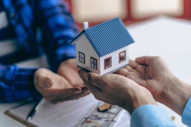 Emlakçı ev satın alma anlaşmasının şartlarını tartışıyor ve müşteriden sözleşmeyi imzalamasını ve evi teslim etmesini istiyor..