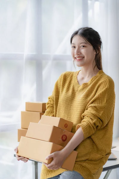 Asian female home-based SME business preparing parcel delivery boxes for online shopping Beginners start small business owners at home. Ordered online with a yellow parcel box. vertical image