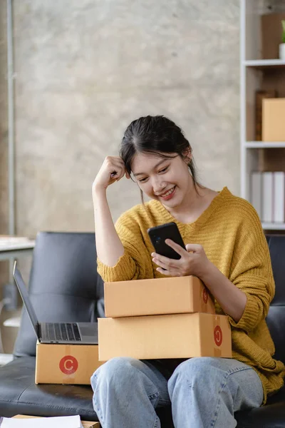 Asian female home-based SME business preparing parcel delivery boxes for online shopping Beginners start small business owners at home. Ordered online with a yellow parcel box. vertical image