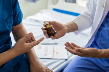 Doktor ve hasta semptomları hastalarla ilaç ve tedavi yöntemleri hakkında tartışıyor, teşhis koyuyor, oturuyor ve konuşuyorlar. Hastane tıbbı konseptinde pencerenin yanındaki masada.