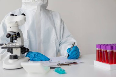 Bir doktorun elinde diğer örneklerin yanında kan testi yapılan küçük bir şişe bulunur. Laboratuvarda çalışırken beyaz üniformalı bir bilim adamının yakın plan fotoğrafını çek..