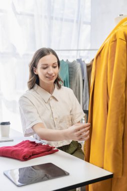 Moda blogcusu konsepti Canlı video, sosyal medya, dijital kamera ile çevrimiçi satış yapmak için kıyafetleri elinde tutan genç kadın..