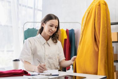 Moda blogcusu konsepti Canlı video, sosyal medya, dijital kamera ile çevrimiçi satış yapmak için kıyafetleri elinde tutan genç kadın..