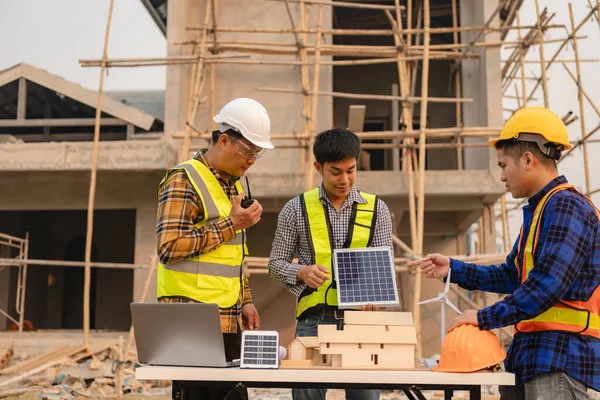 Architects and engineers work together on building sketches and discuss at the construction site with wind turbine blades and solar chases, greener alternative energy for the future.