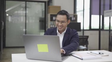 Masada çalışan gülümseyen Asyalı erkek muhasebeci hesap makinesi yöneticisini kullanarak yıllık mali vergilerini hesaplıyor şirketlerin mali muhasebe evraklarını inceliyor.