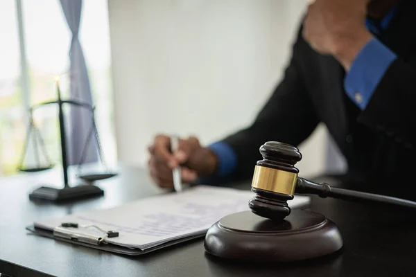 Middle-aged male lawyer working with legal contract documents in court room Justice with tee hammer and black scales on table, law judge consulting and legal services concept