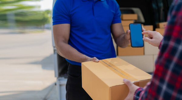 Smiling african american courier holding cardboard box delivering parcel to business customer signing electronic signature POD device on smartphone