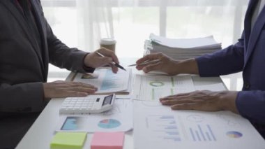 Genç işadamı, Asyalı borsa simsarı ya da satış vergisi komisyoncusu, kısa tanıtım ve eliyle grafik raporuna işaret ediyor. Bütçe çizelgelerini veya hukuki sonuçları gösteren masalardaki müşterilerle tartışın.