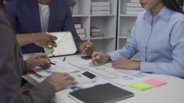 Genç işadamı, Asyalı borsa simsarı ya da satış vergisi komisyoncusu, kısa tanıtım ve eliyle grafik raporuna işaret ediyor. Bütçe çizelgelerini veya hukuki sonuçları gösteren masalardaki müşterilerle tartışın.