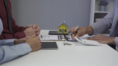 Dosyasında ev detaylarını gösteren emlakçı genç Asyalı bir çifte yeni bir ev almakla ve koşullar sunmakla ve ev satın alma sözleşmesi ve ev sigortası kavramını imzalamakla ilgileniyor.