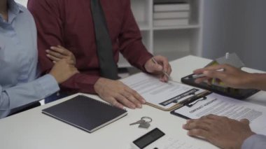 Dosyasında ev detaylarını gösteren emlakçı genç Asyalı bir çifte yeni bir ev almakla ve koşullar sunmakla ve ev satın alma sözleşmesi ve ev sigortası kavramını imzalamakla ilgileniyor.