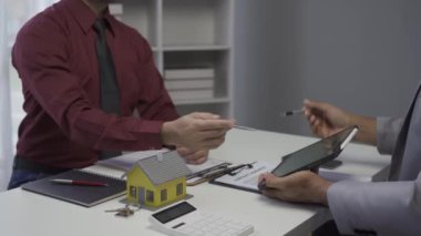 Dosyasında ev detaylarını gösteren emlakçı genç Asyalı bir çifte yeni bir ev almakla ve koşullar sunmakla ve ev satın alma sözleşmesi ve ev sigortası kavramını imzalamakla ilgileniyor.