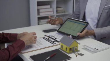 Dosyasında ev detaylarını gösteren emlakçı genç Asyalı bir çifte yeni bir ev almakla ve koşullar sunmakla ve ev satın alma sözleşmesi ve ev sigortası kavramını imzalamakla ilgileniyor.