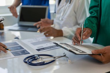 Beyaz laboratuvar önlüklü ve ameliyat önlüklü doktorlarla toplantılar, masalarda oturmak, tıbbi hasta kayıtlarını tartışmak, çeşitlilik gösterileri, işbirliği, veri analizi için takım çalışması veya atölyeler üzerinde çalışmak..