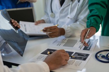 Beyaz laboratuvar önlüklü ve ameliyat önlüklü doktorlarla toplantılar, masalarda oturmak, tıbbi hasta kayıtlarını tartışmak, çeşitlilik gösterileri, işbirliği, veri analizi için takım çalışması veya atölyeler üzerinde çalışmak..