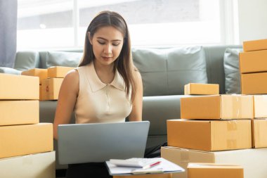 Küçük işletme girişimcisi, kurucu ya da serbest çalışan Asyalı bir kadın, paket kutuları ve dizüstü bilgisayarlarla çalışan başarılı bir Asyalı kadın, paketleme kutularıyla, çevrimiçi pazarlaması ve taşımacılığıyla.