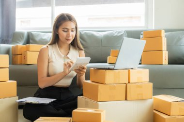Küçük işletme girişimcisi, kurucu ya da serbest çalışan Asyalı bir kadın, paket kutuları ve dizüstü bilgisayarlarla çalışan başarılı bir Asyalı kadın, paketleme kutularıyla, çevrimiçi pazarlaması ve taşımacılığıyla.