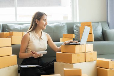 Küçük işletme girişimcisi, kurucu ya da serbest çalışan Asyalı bir kadın, paket kutuları ve dizüstü bilgisayarlarla çalışan başarılı bir Asyalı kadın, paketleme kutularıyla, çevrimiçi pazarlaması ve taşımacılığıyla.
