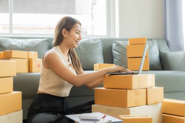 Küçük işletme girişimcisi, kurucu ya da serbest çalışan Asyalı bir kadın, paket kutuları ve dizüstü bilgisayarlarla çalışan başarılı bir Asyalı kadın, paketleme kutularıyla, çevrimiçi pazarlaması ve taşımacılığıyla.